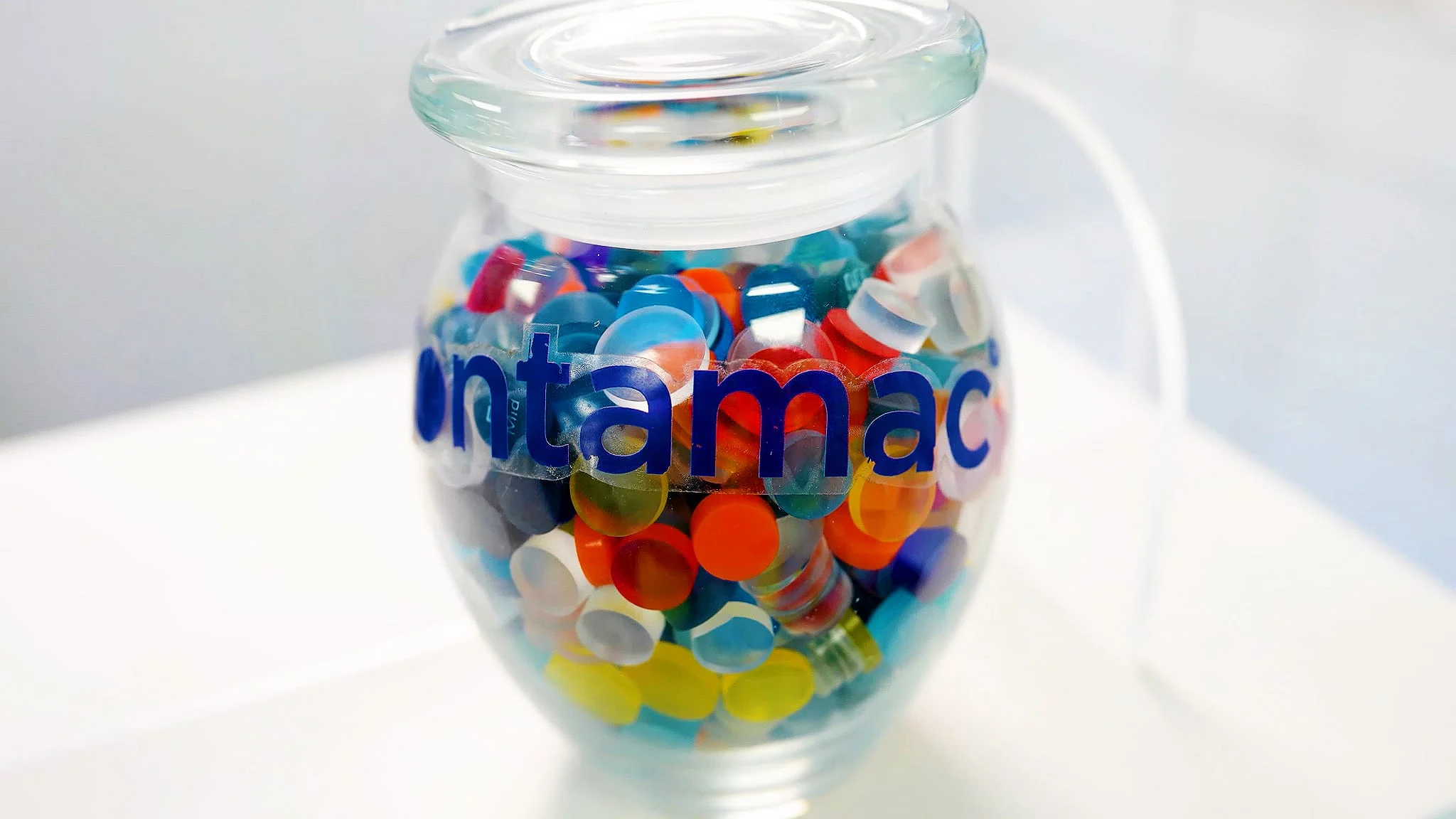 A branded jar of colorful finished Contamac lens buttons