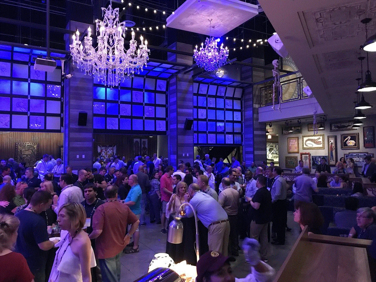 Conference attendees mingling at the evening reception in the House of Blues Anaheim, under crystal chandeliers and blue lights