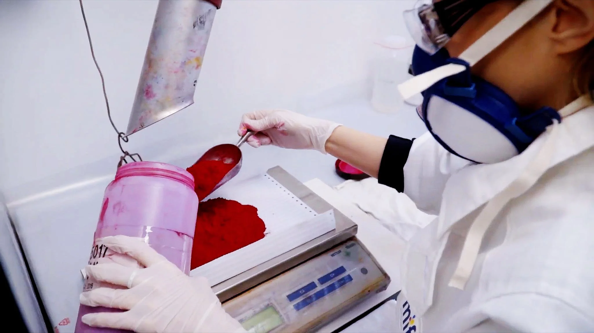 A technician in protective equipment weighing red pigment powder