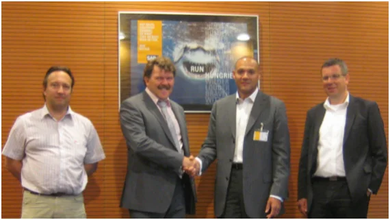 Four men at SAP Netherlands, two of them shaking hands in front of an SAP poster