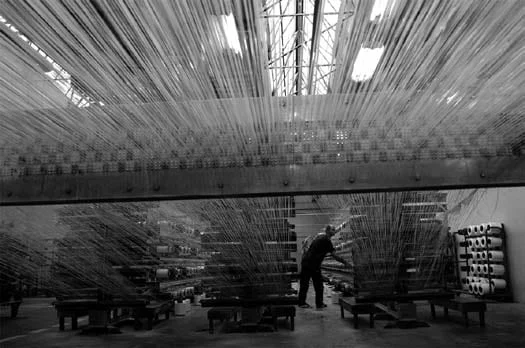 Operator working among rows of yarn creels in a polypropylene yarn production hall