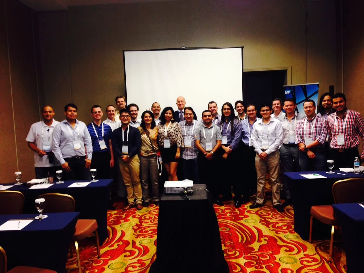 About 25 attendees standing in front of a projection screen in a hotel conference room