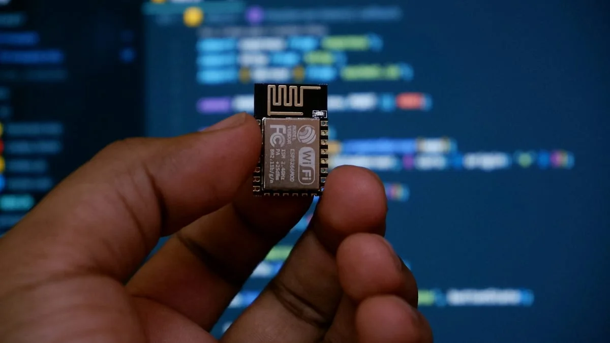A small wireless module held in front of a screen of code