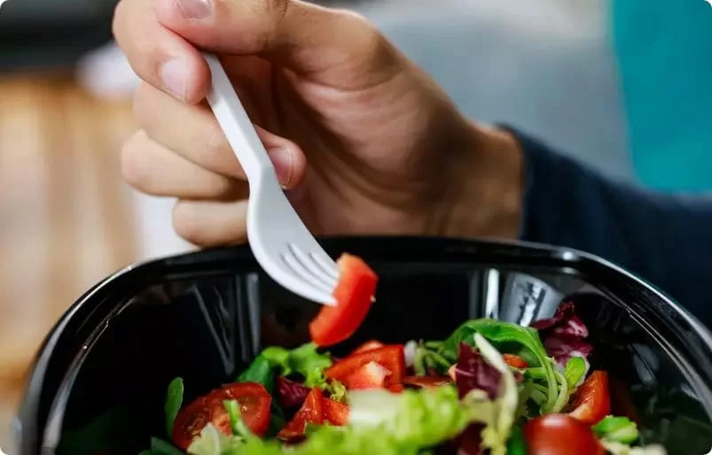 A hand using a plastic fork to eat a salad